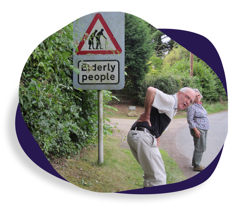 older man holding his back in mock pain at an elderly people crossing sign