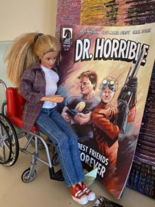 a barbie in a wheelchair looking at a Dr. Horrible comic
