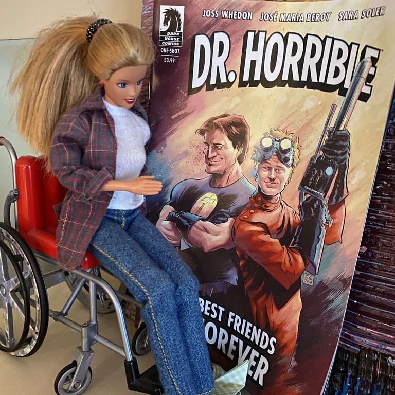 a barbie in a wheelchair looking at a Dr. Horrible comic